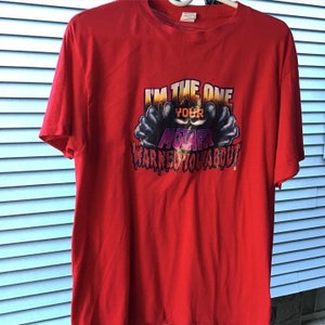 May include: A red t-shirt with the text "I'M THE ONE YOUR MOTHER WARNED YOU ABOUT" in a stylized font. The graphic includes a monster-like figure with dark hands reaching out.