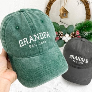 Peut inclure: Deux casquettes de baseball ajustables, une verte avec le texte "GRANDPA EST. 2025" et une grise avec le texte "GRANDAD EST. 2025".