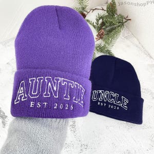 May include: Two knit beanies, one purple and one navy blue. The purple beanie says "AUNTIE EST. 2026" in white lettering. The navy blue beanie says "UNCLE EST. 2026" in white lettering. Both beanies have a folded brim.