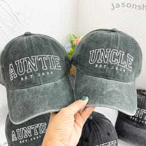 Könnte beinhalten: Drei dunkelgraue Baseballkappen aus Denim mit weiß gesticktem Text. Die Kappen tragen die Aufschrift "Auntie EST. 2024", "Uncle EST. 2024" und "Auntie EST. 2023".