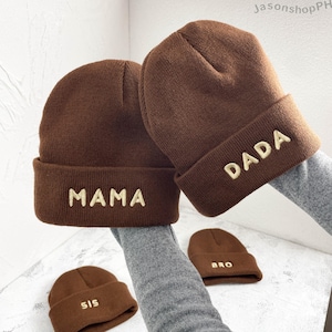 May include: Brown knit beanies with embroidered text. Two larger beanies display "MAMA" and "DADA", while two smaller beanies show "SIS" and "BRO". The hats are a warm brown color, perfect for family matching.
