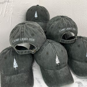May include: A collection of dark gray baseball caps. Each cap features a white embroidered tree on the front and the text "CAMP LIEBO 2026" on the back. The caps have a distressed, vintage look.