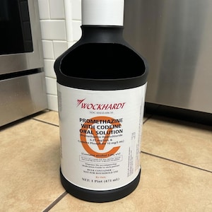 May include: A black and white bottle of Wockhardt Promethazine with Codeine Oral Solution. The label includes the text "Promethazine Hydrochloride 6.25 mg/5mL & Codeine Phosphate 10 mg/5 mL" and "NET: 1 Pint (473 mL)."