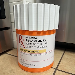 May include: An orange and white 11.34-litre trashcan with a white lid. The trashcan has the text "REVAMP3D RX" and "400 oz TRASHCAN" printed on it. The trashcan is cylindrical and has a white, ridged lid.
