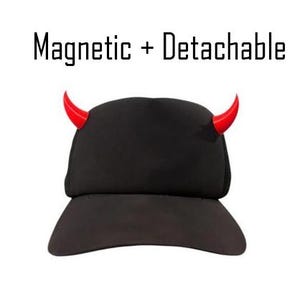 Op de afbeelding: Zwarte baseballcap met rode duivelshoorns. De tekst "Magnetic + Detachable" staat boven de cap. De cap heeft een gebogen klep en een gestructureerde kroon. De hoorns zijn gebogen en wijzen omhoog.