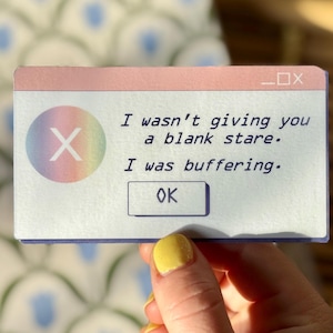 May include: A pink and blue computer error message with a rainbow X icon and the text "I wasn't giving you a blank stare. I was buffering." with an OK button.