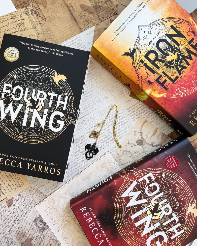 May include: Three fantasy novels with a dragon theme. The books are titled "Fourth Wing" and "Iron Flame". The books are on a table with a gold bookmark and a dragon charm.