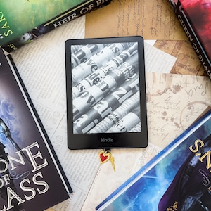 Puede incluir: Un lector electrónico en blanco y negro con una pantalla que muestra un artículo de periódico. El lector electrónico está etiquetado como "kindle" y tiene un marcador en forma de corazón rojo adjunto.