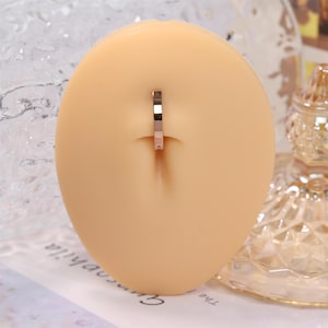 May include: A gold-toned belly button ring on a flesh-toned display stand.