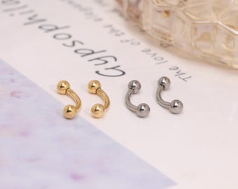 Könnte beinhalten: Vier gebogene Barbell-Ohrringe. Zwei sind goldfarben und zwei silberfarben. Jeder Ohrring hat an jedem Ende eine kleine Kugel. Die Ohrringe werden auf einer weißen Oberfläche mit Text im Hintergrund präsentiert.