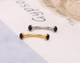 Könnte beinhalten: Zwei gebogene Augenbrauenpiercings. Eines ist goldfarben, das andere silberfarben. Jeder Ring hat an jedem Ende einen kleinen, runden, schwarzen Stein. Der Schmuck wird auf einer weißen Oberfläche präsentiert.