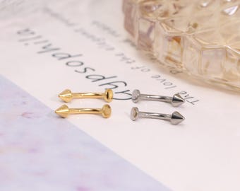 Könnte beinhalten: Nahaufnahme von vier kleinen Ohrringen. Zwei sind goldfarben und zwei sind silberfarben. Jeder Ohrring hat einen geraden Stab mit einer flachen Scheibe an einem Ende und einem spitzen Kegel am anderen Ende. Die Ohrringe liegen auf einer weißen Oberfläche.