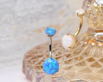 May include: A silver belly button ring with two blue opal stones. The stones are round and have a sparkly finish.