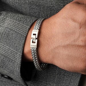 May include: A silver chain bracelet with a personalized engraved clasp. The clasp reads "Williams" and "Emma" with a heart symbol between the names.
