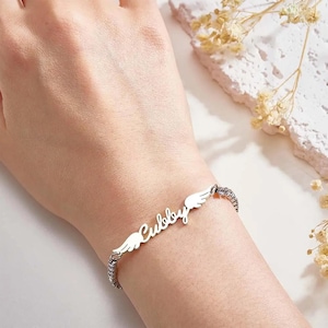 Op de afbeelding: Een zilveren armband met een naamplaatje waarop "Cubby" staat met engelenvleugels aan beide kanten.