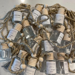 May include: A collection of small glass bottles with wooden tops and string hangers. The bottles are filled with a clear liquid and have labels with different scents, including Lavender, Acai Berry Satin, Beach Daisies, Pink Sugar, and Apple Mango.