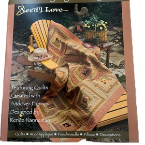 May include: The cover of a book titled "Daylily Days" shows a quilt draped over a wooden chair. The quilt is in shades of brown, orange, and green. The book cover also includes the text "Featuring Quilts Created with Andover Fabrics Designed by Renée Nanneman."