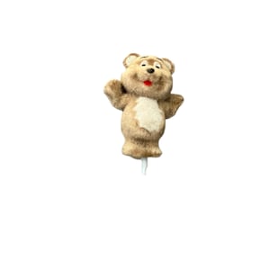May include: A brown teddy bear figurine with a white chest and a red mouth. The bear has its arms outstretched and is mounted on a white stick. The figurine is likely a cake topper or decorative item.