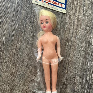 May include: A 7.5-inch doll with blonde hair, blue eyes, and white shoes, packaged in a clear plastic bag. The doll is nude and has a tag that reads "WESTRIM CRAFTS".