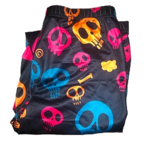 May include: Black pajama pants with a repeating pattern of colorful skulls in orange, pink, blue, and yellow. The skulls have various expressions and are scattered across the fabric.