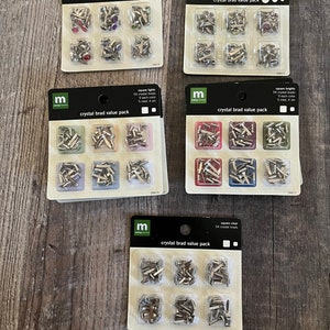 Puede incluir: Cuatro paquetes de tachuelas de cristal en diferentes colores y tamaños. Cada paquete contiene 54 o 60 tachuelas e incluye una variedad de tamaños. Las tachuelas son plateadas con cristales transparentes, rojos, azules y verdes.