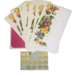 May include: Vintage stationery set with a fruit basket design, including grapes, apples, and pears. The set includes a pink envelope and gold foil seals. Ideal for letters or notes. The stationery is in a fan shape.