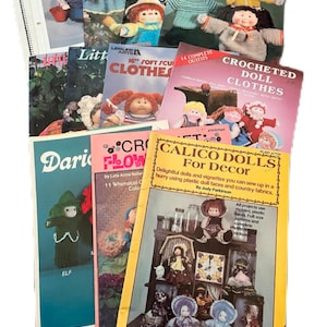 May include: A selection of vintage crochet pattern books, showcasing doll clothes and craft projects. The covers feature colourful illustrations of crocheted dolls and outfits. Titles include "Calico Dolls For Decor" and "Crocheted Doll Clothes."