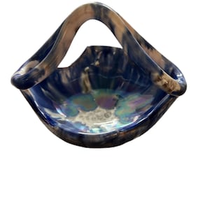 May include: A blue ceramic basket with a handle. The basket has a wide, shallow bowl shape with iridescent accents in the center. The handle is a lighter color with darker blue streaks.