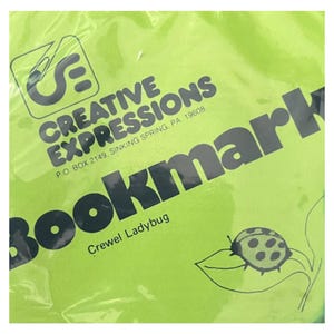 以下が含まれることがあります： ライムグリーンのパッケージには、黒い文字で「Creative Expressions, P.O. Box 2149, Sinking Spring, PA. 19608」と、大きな太字で「Bookmark」と書かれています。その下には「Crewel Ladybug」という文字と、葉の上にいるテントウムシの線画が描かれています。