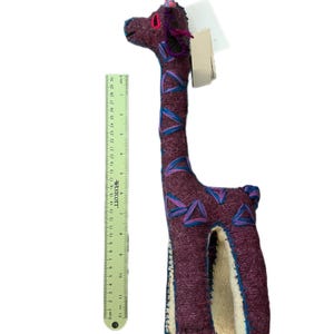 Pode incluir: Um brinquedo de girafa de pel&uacute;cia feito &agrave; m&atilde;o, principalmente bord&ocirc; com detalhes azuis e rosa. A girafa tem aproximadamente 30 cm de altura, com um pesco&ccedil;o longo e um design estampado. Possui uma etiqueta anexada.