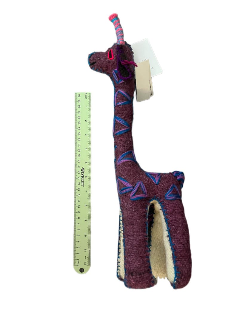 Pode incluir: Um brinquedo de girafa de pel&uacute;cia feito &agrave; m&atilde;o, principalmente bord&ocirc; com detalhes azuis e rosa. A girafa tem aproximadamente 30 cm de altura, com um pesco&ccedil;o longo e um design estampado. Possui uma etiqueta anexada.