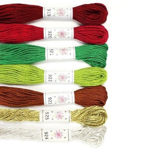 May include: A selection of embroidery floss in various colors, including red, green, brown, gold, and silver. Each skein is labeled with a number and a floral design. The floss is arranged on a white background.