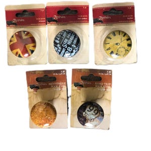 Könnte beinhalten: Sechs verschiedene Buchstützen mit verschiedenen Designs. Die Buchstützen sind rund und zeigen eine Vielzahl von Bildern, darunter eine Union Jack-Flagge, ein Zifferblatt, eine Weltkarte und ein Vintage-Straßenschild. Jede Buchstütze ist in einer durchsichtigen Plastiktüte mit einem braunen und roten Etikett verpackt, auf dem "7gypsies" steht.