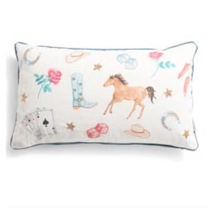May include: Rectangular white pillow with a blue border, featuring a watercolor design of cowboy-themed elements. The design includes a horse, cowboy boots, playing cards, roses, and stars.