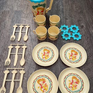 Puede incluir: Un juego de té vintage de Cabbage Patch Kids. El juego incluye una jarra con tapa azul, cuatro tazas, cuatro platos, seis posavasos azules con forma de flor y tres juegos de tenedores y cucharas. Los platos presentan un gráfico de Cabbage Patch Kids.