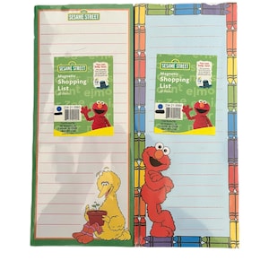 May include: Two Sesame Street magnetic shopping list notepads. One notepad features Big Bird holding a plant, and the other features Elmo. The notepads have lined paper and are bordered with green and crayon designs.