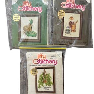 May include: Three Jiffy Stitchery cross-stitch kits in plastic packaging. The kits feature framed designs of an onion and peppers, spices, and an asparagus fern. Each kit includes a frame.