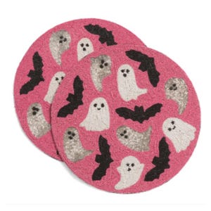 May include: Two round pink beaded placemats with a Halloween theme. Each placemat features white and gray ghosts and black bats. The placemats are decorated with small beads.