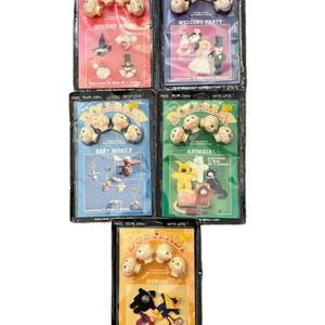 May include: Five packages of Make Your Own Doll Baby craft kits featuring plastic doll heads and instructions. The sets are titled Holiday Heads, Wedding Party, Baby Mobile, Animals, and Heroes, each containing components to create four distinct figures.