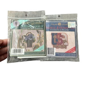 Puede incluir: Dos kits de adornos de cuentas de vidrio contadas Mill Hill sellados. Uno se titula "Spring Bouquet II" con un diseño floral. El otro es "Political & Olympic" con un diseño geométrico. Ambos kits incluyen cuentas, papel perforado e instrucciones.