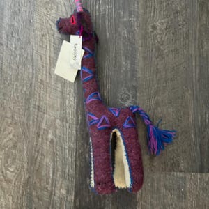 Pode incluir: Um brinquedo de girafa de pel&uacute;cia feito &agrave; m&atilde;o em tons de roxo, azul e rosa. A girafa tem um pesco&ccedil;o longo e uma cauda tran&ccedil;ada. A etiqueta diz "Twoolies".