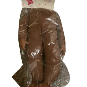 May include: A brown doll in a clear plastic bag. The doll has a full body with arms and legs. The packaging has the text "Sweet Love Kids" and a small illustration of a child.