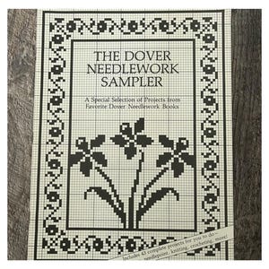 Puede incluir: Un libro antiguo titulado "The Dover Needlework Sampler" con un diseño floral en blanco y negro. La portada presenta el título y el texto "A Special Selection of Projects from Favorite Dover Needlework Books". Incluye 43 proyectos completos.