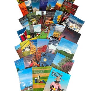 Puede incluir: Una pila de revistas Farm & Ranch con diferentes portadas que muestran paisajes rurales, animales de granja y escenas agrícolas. Las revistas están dispuestas en forma de abanico, con la revista superior mostrando a un vaquero montando a caballo.
