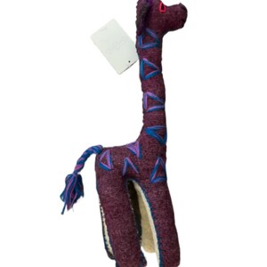 Pode incluir: Um brinquedo de pel&uacute;cia de girafa artesanal em tons de bord&ocirc;, azul e rosa. A girafa apresenta um pesco&ccedil;o longo, padr&otilde;es triangulares e uma cauda tran&ccedil;ada. Possui uma etiqueta.