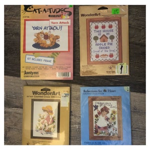 May include: Four vintage counted cross-stitch kits. One kit features a cartoon cat with the text "Yarn Attack!!". Another says "This House Is In Apple Pie Order". The other two kits feature children.