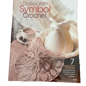 May include: A book titled "Doilies With Symbol Crochet" featuring a close-up of a crocheted doily and a white pitcher. The book cover includes the text "7 Fabulous Designs using traditional instructions and easy-to-follow symbols." and the number 871241.