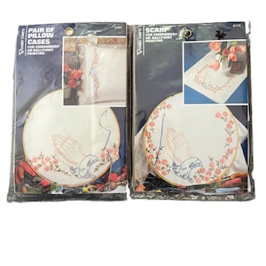 May include: Two sealed craft kits by Vogart Crafts. The left package contains a pair of pillowcases for embroidery or ballpoint painting, featuring a praying hands design. The right package contains a scarf for embroidery or ballpoint painting.