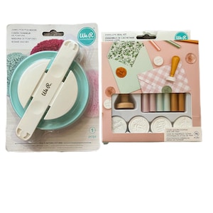 May include: Two craft kits: a jumbo pom pom maker and an envelope seal kit. The pom pom maker is white and teal, measuring 5 inches (127 mm). The seal kit includes wax sticks, stamps, and decorative elements, all in a pink box.