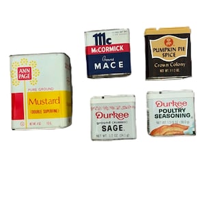May include: A collection of vintage spice tins, including McCormick Ground Mace, Ann Page Mustard, Durkee Sage, Durkee Poultry Seasoning, and Pumpkin Pie Spice. The tins are rectangular with various colors and text labels.